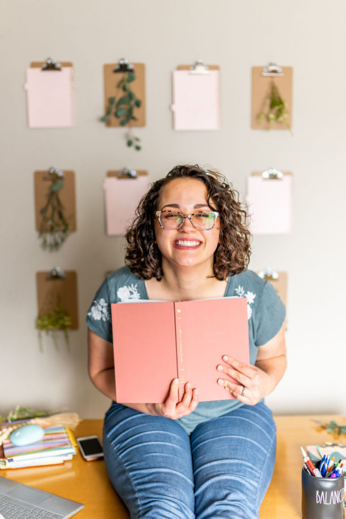 website designer and SEO expert holding a book to her chest while sitting on her desk and laughing 